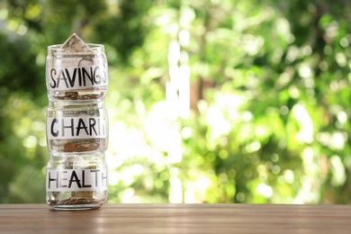 Glass jars with money for different needs on table against blurred background, space for text