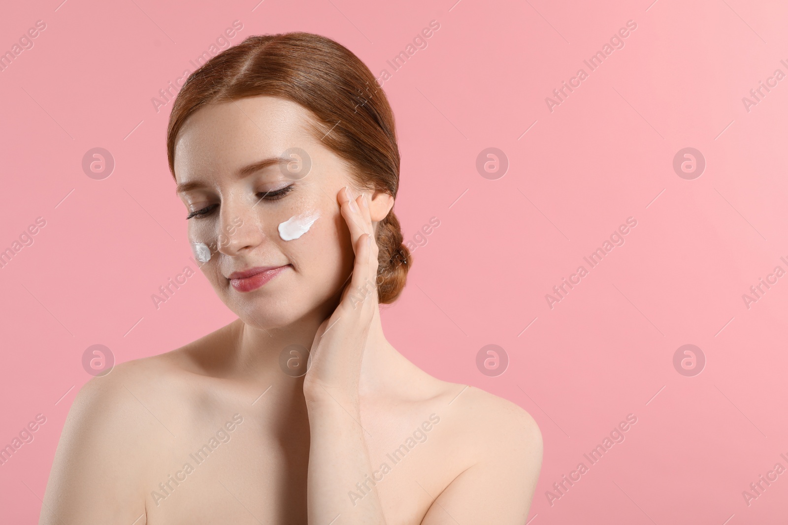 Photo of Beautiful woman with freckles and cream on her face against pink background. Space for text