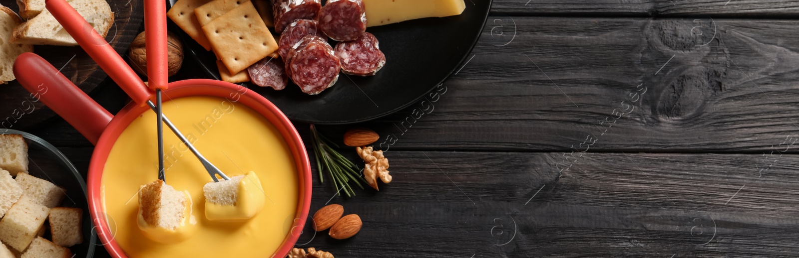 Image of Pot of tasty cheese fondue and snacks on black wooden table, flat lay with space for text. Banner design