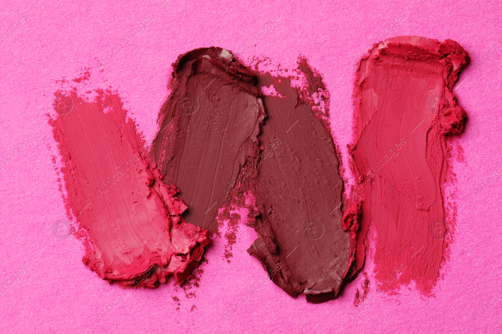 Photo of Smears of bright lipsticks on pink background, top view