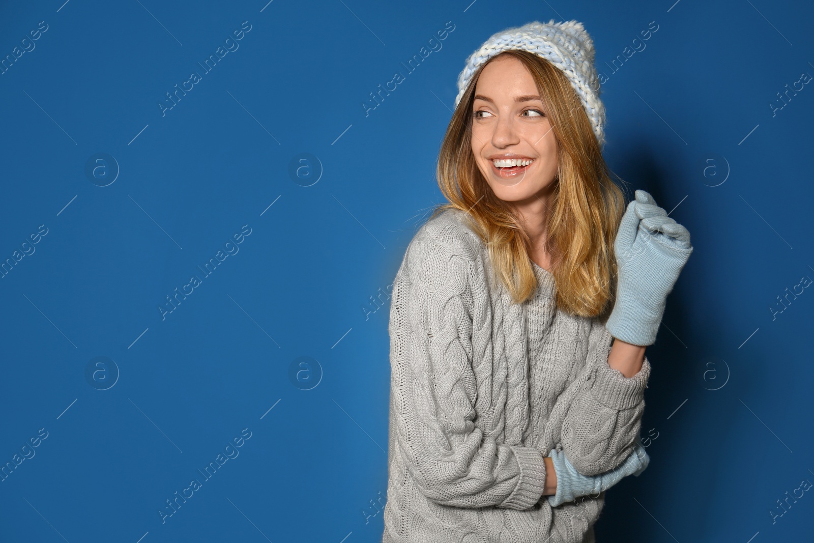 Image of Happy young woman wearing warm sweater, knitted hat and mittens on blue background. Space for text