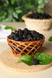 Photo of Wicker basket of delicious ripe black mulberries on white table
