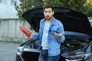 Photo of Puzzled man holding red containermotor oil near car outdoors