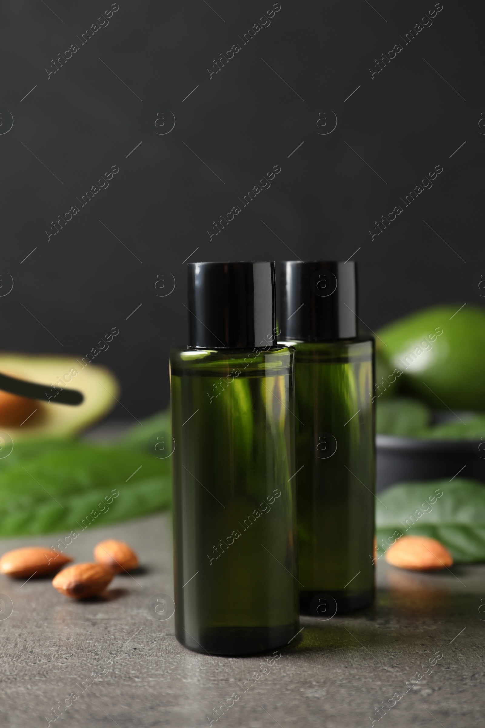 Photo of Bottles of avocado essential oil and almonds on grey table
