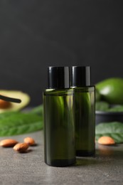 Bottles of avocado essential oil and almonds on grey table