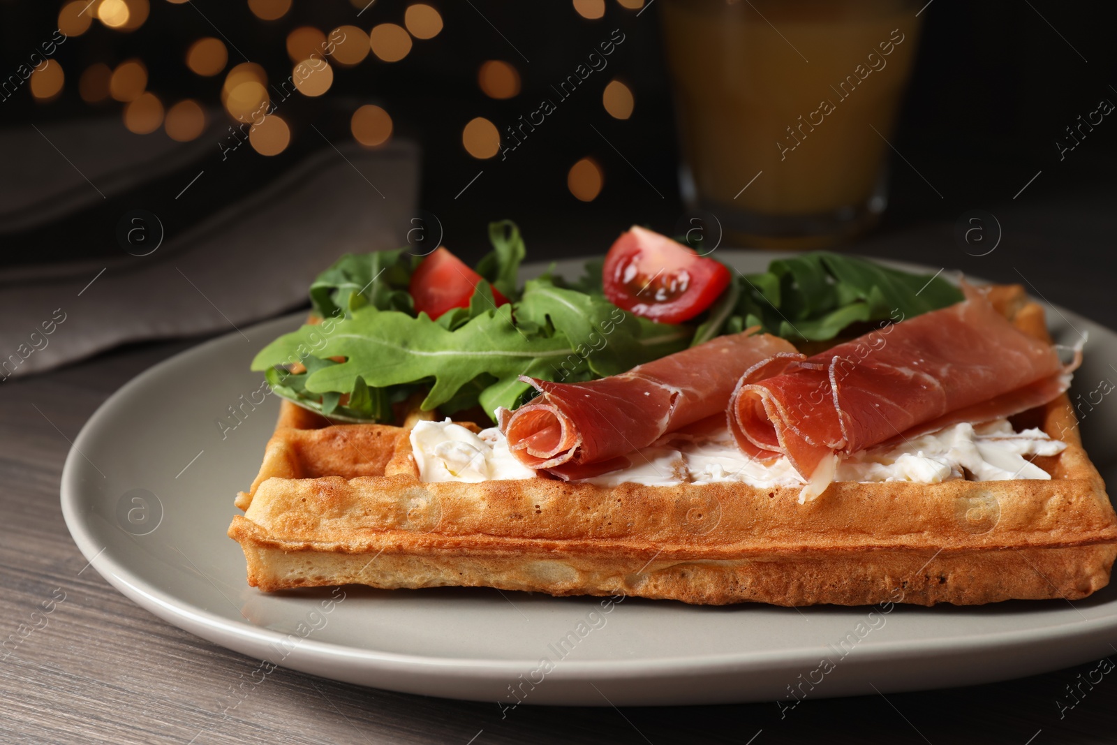 Photo of Delicious waffle with cheese, prosciutto, tomatoes and arugula on wooden table