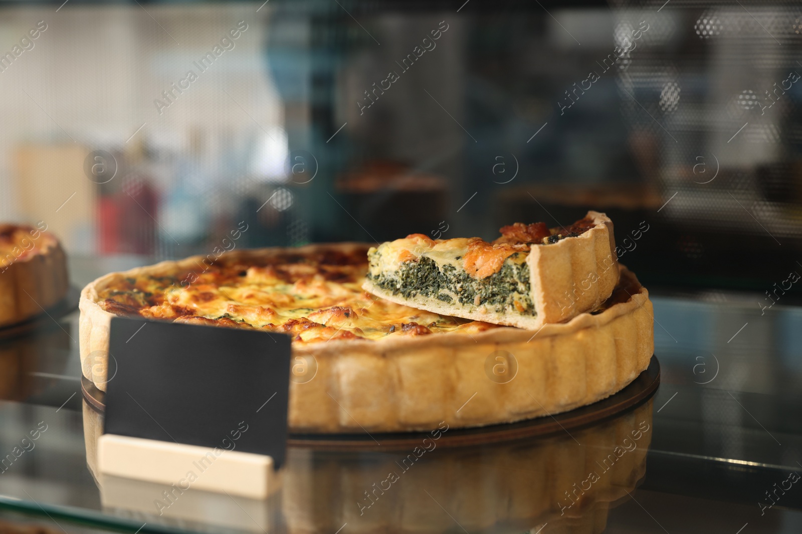 Photo of Delicious quiche with salmon and spinach on counter in bakery shop, closeup. Space for text
