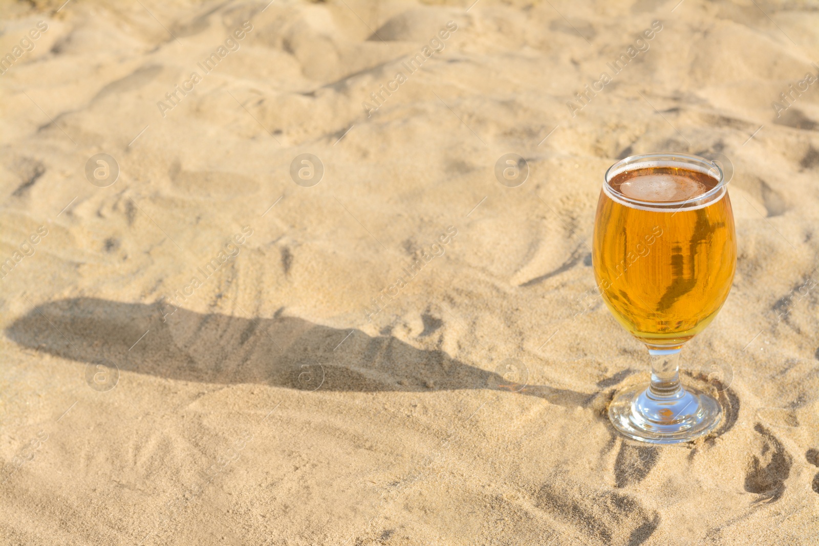 Photo of Glass of cold beer on sandy beach. Space for text