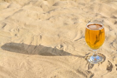 Glass of cold beer on sandy beach. Space for text