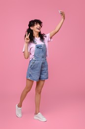 Photo of Beautiful young woman taking selfie on pink background