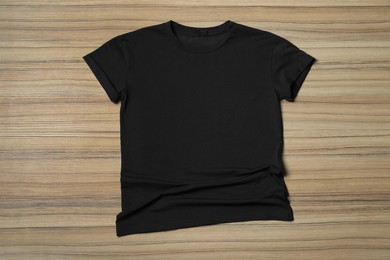 Stylish black T-shirt on wooden table, top view