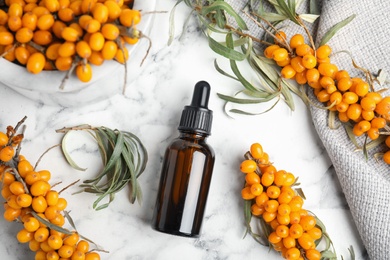 Natural sea buckthorn oil and fresh berries on white marble table, flat lay