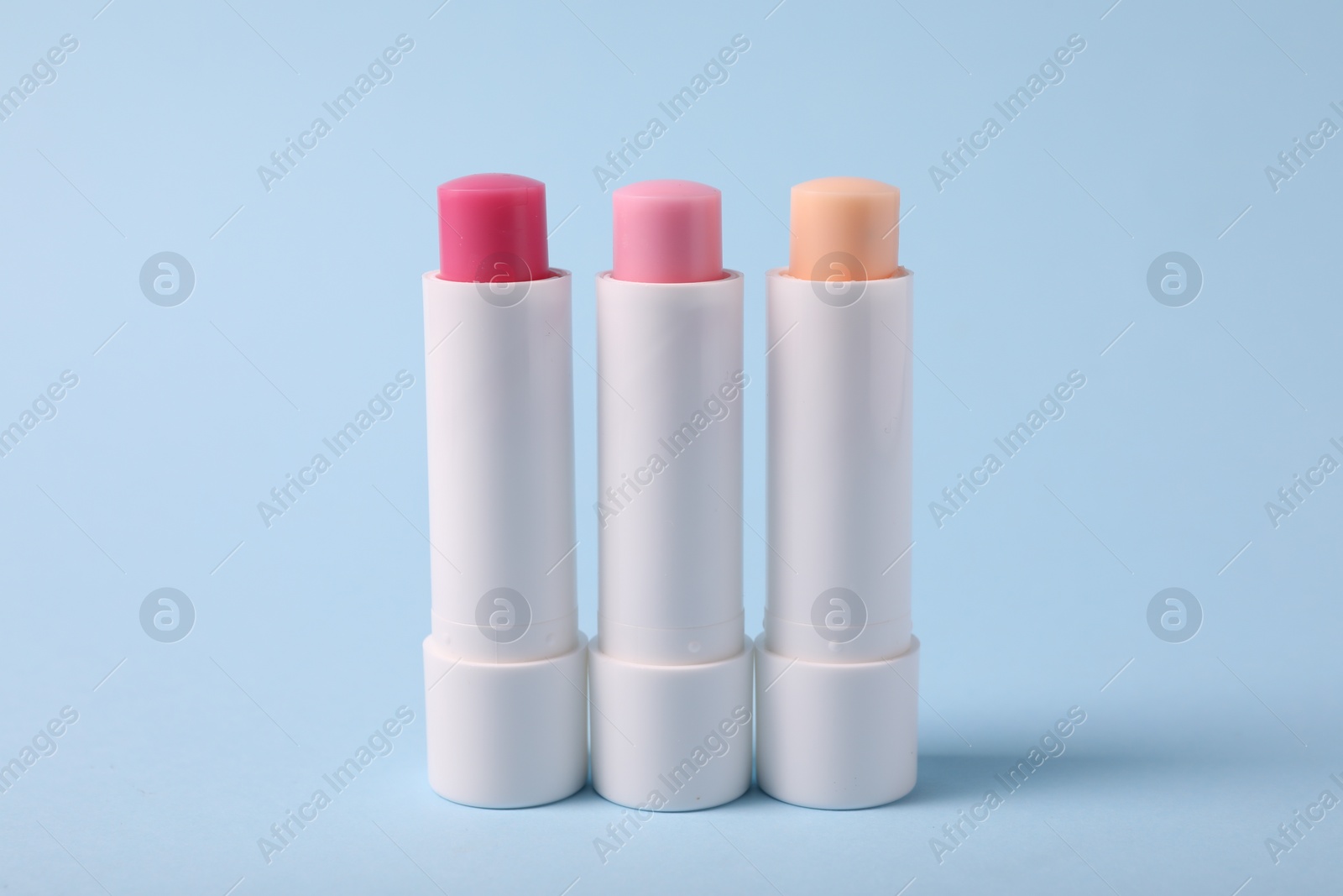 Photo of Different lip balms on light blue background