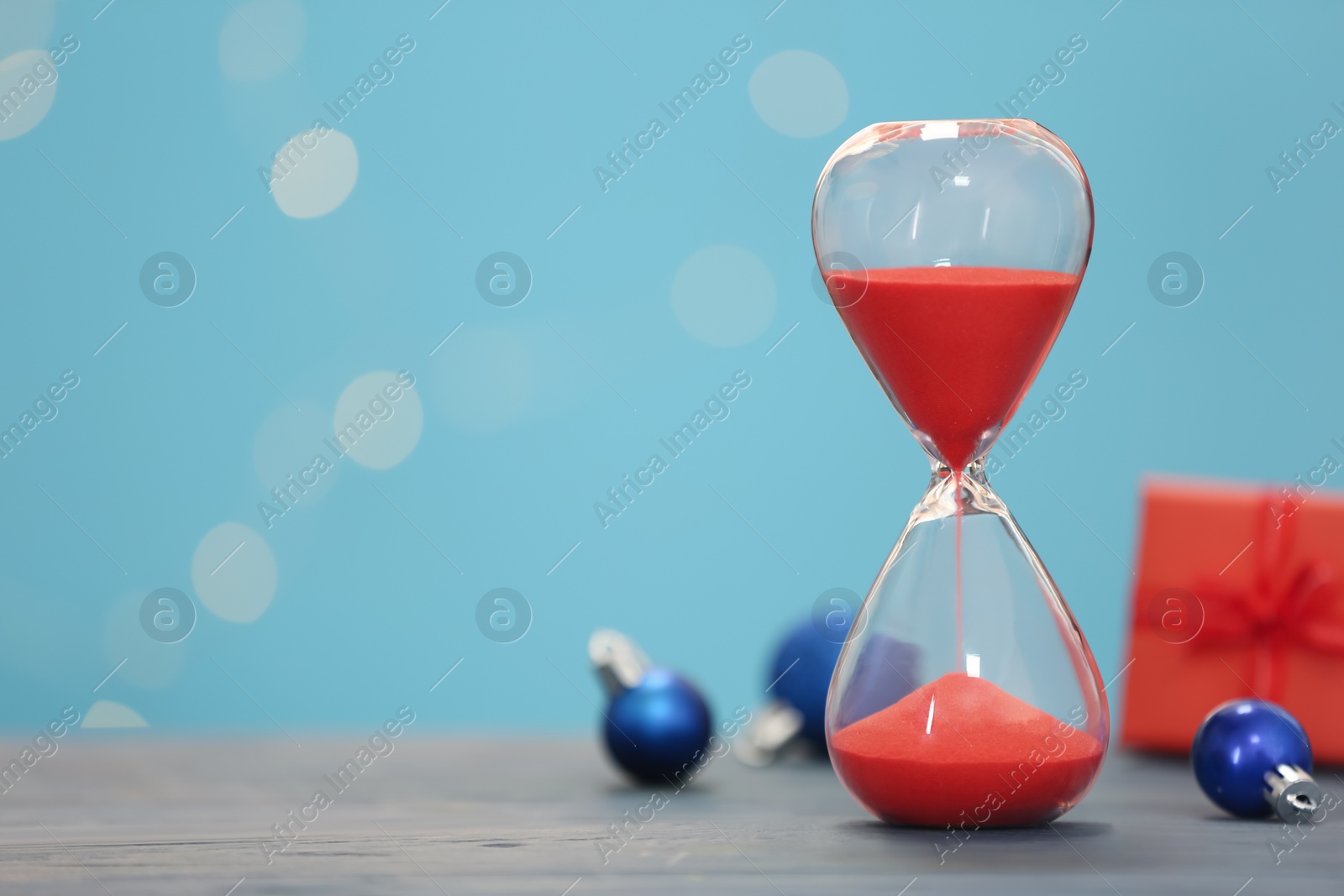 Photo of Hourglass and decor on grey table against blurred lights, space for text. Christmas countdown