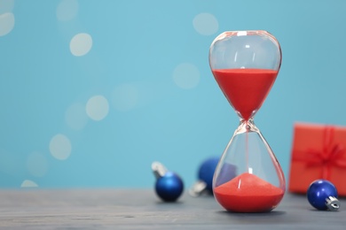 Photo of Hourglass and decor on grey table against blurred lights, space for text. Christmas countdown