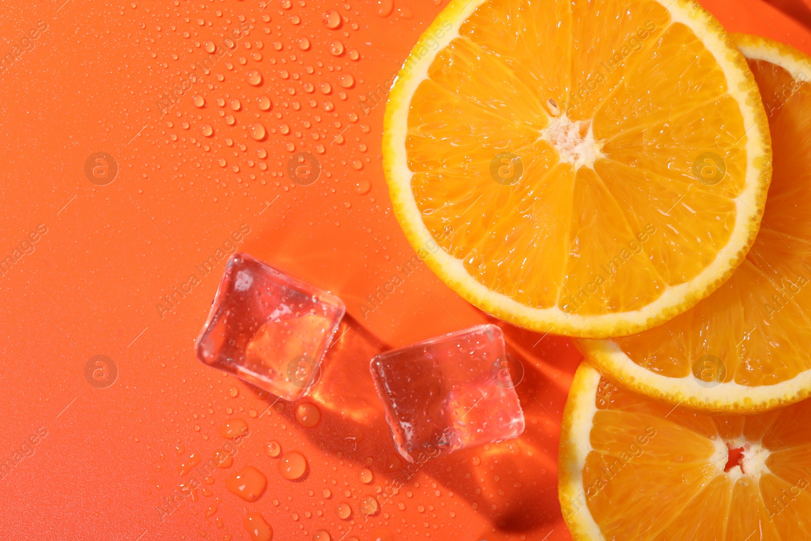 Photo of Slices of juicy orange and ice cubes on terracotta background, flat lay. Space for text