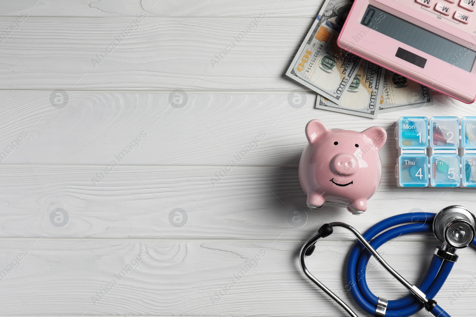 Photo of Pale pink ceramic piggy bank, stethoscope and pills on white wooden table, flat lay with space for text. Medical insurance