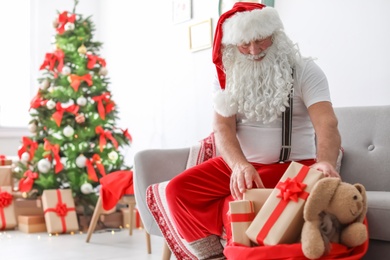 Authentic Santa Claus packing gifts into bag indoors