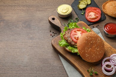 Delicious burger with beef patty and ingredients on wooden table, space for text