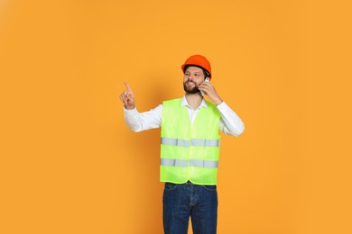 Man in reflective uniform talking on smartphone against orange background