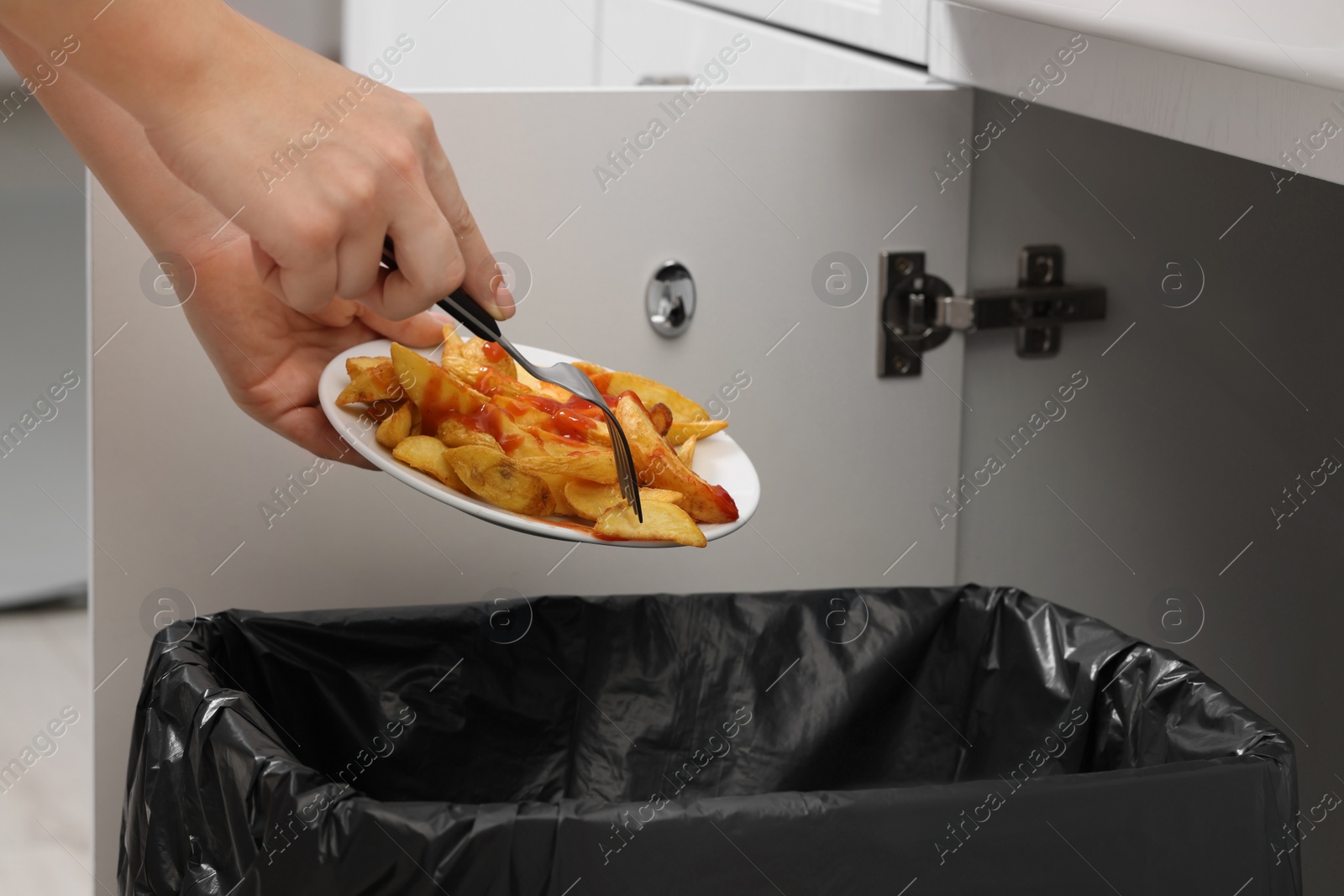 Photo of Woman throwing baked potato with ketchup into bin indoors, closeup