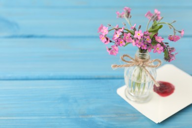 Beautiful pink forget-me-not flowers in glass bottle and envelope on light blue wooden table. Space for text