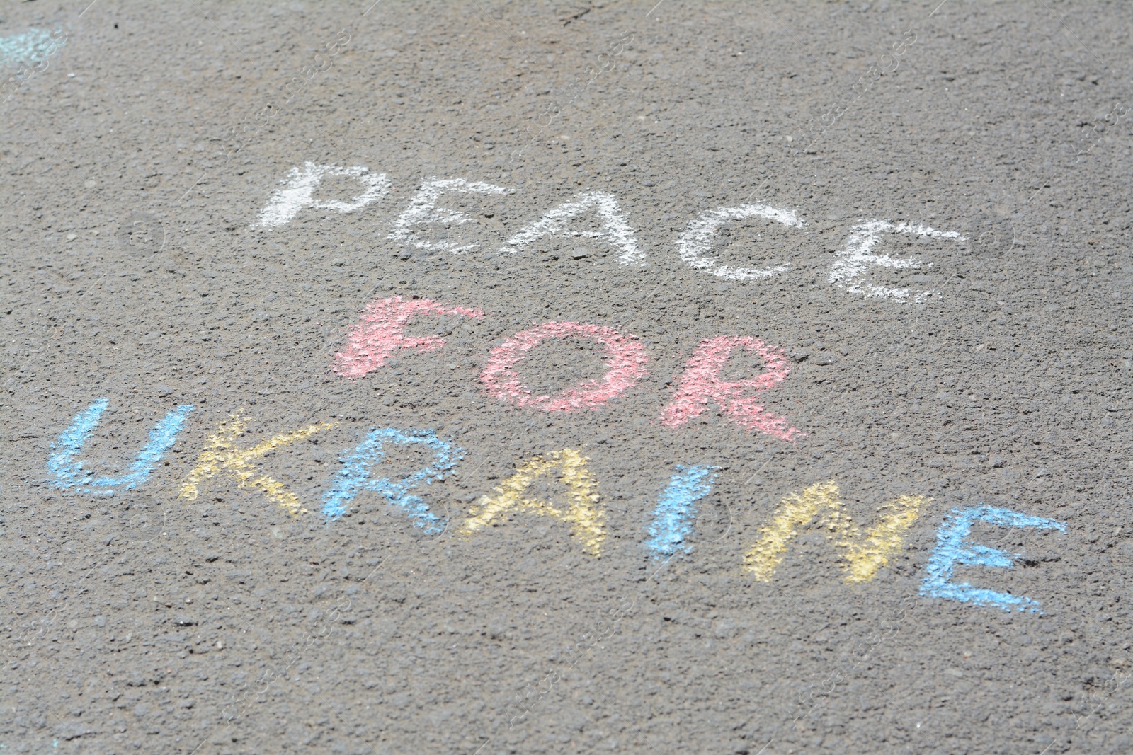 Photo of Words Peace For Ukraine written with colorful chalks on asphalt outdoors