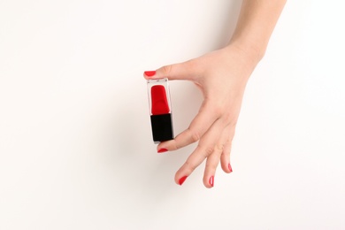 Photo of Woman with red manicure holding nail polish bottle on white background, closeup