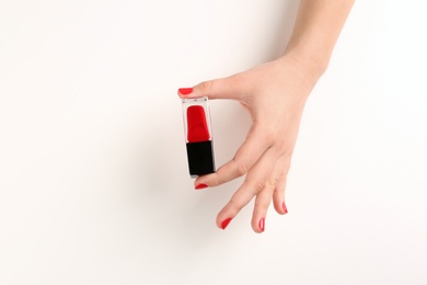 Woman with red manicure holding nail polish bottle on white background, closeup