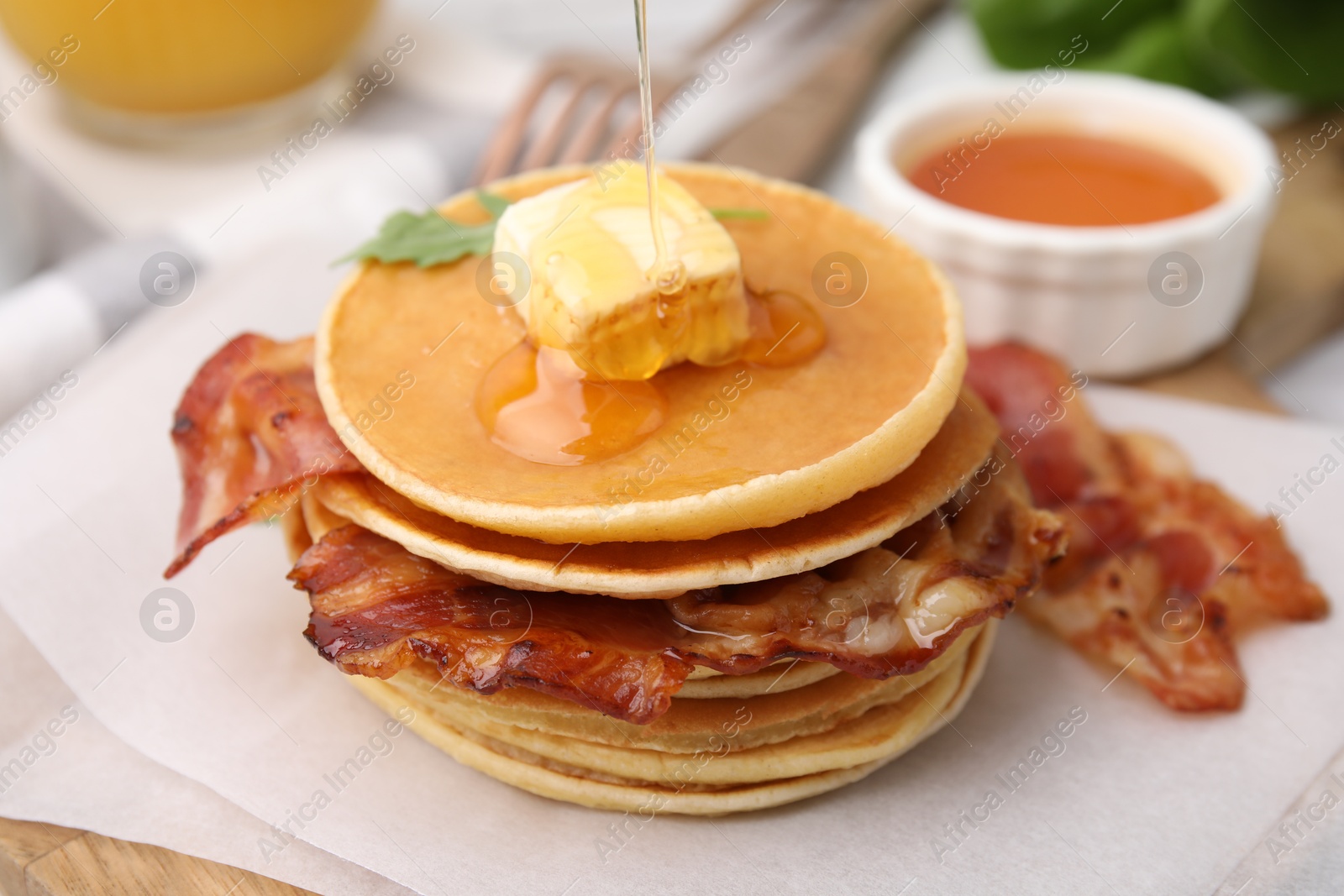 Photo of Pouring honey onto delicious pancakes with bacon at table, closeup