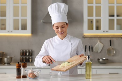 Photo of Professional chef putting cut onion into bowl at white marble table indoors