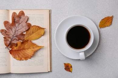 Cup of hot drink, book and autumn leaves on light grey textured table, flat lay