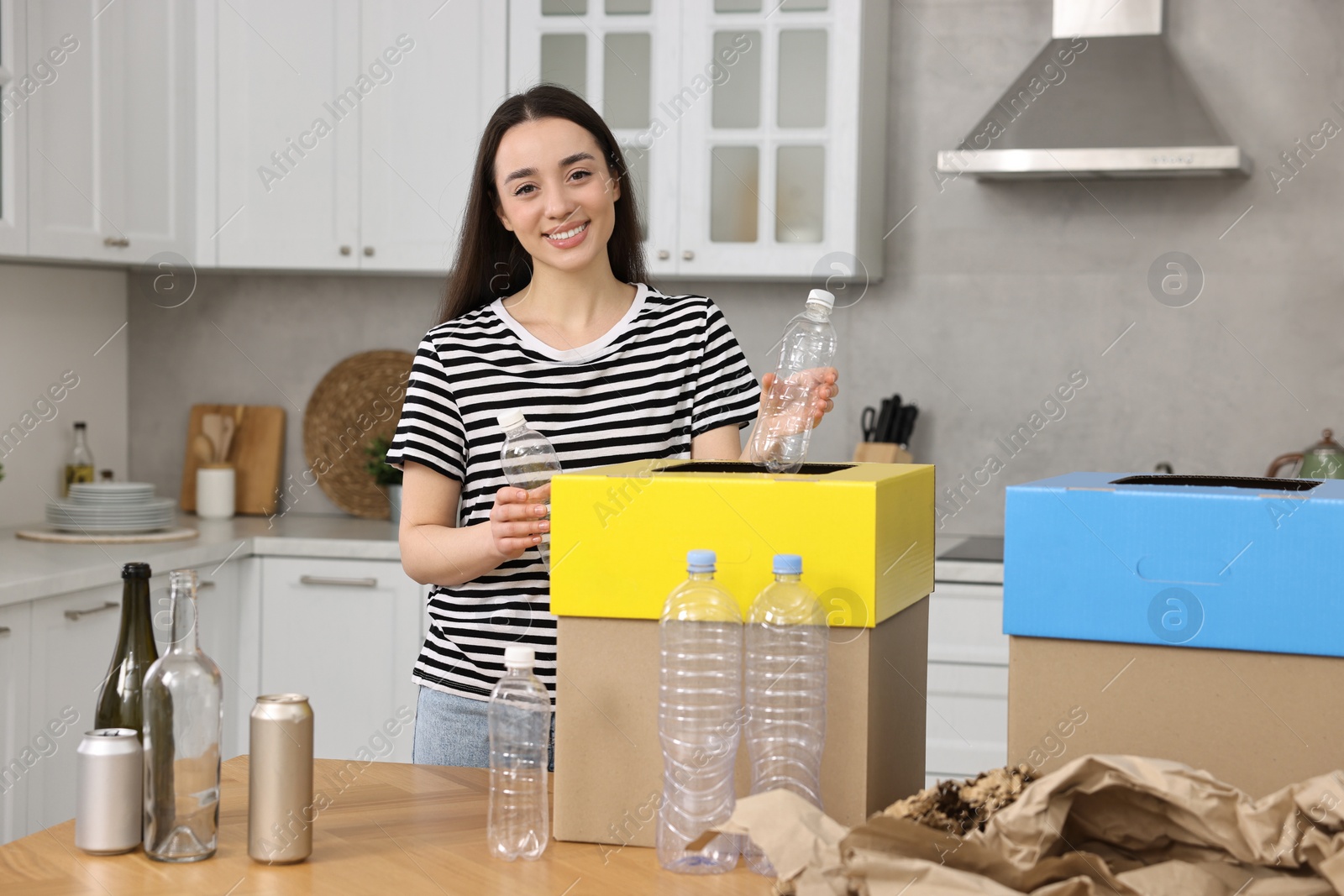 Photo of Smiling woman separating garbage at table in kitchen