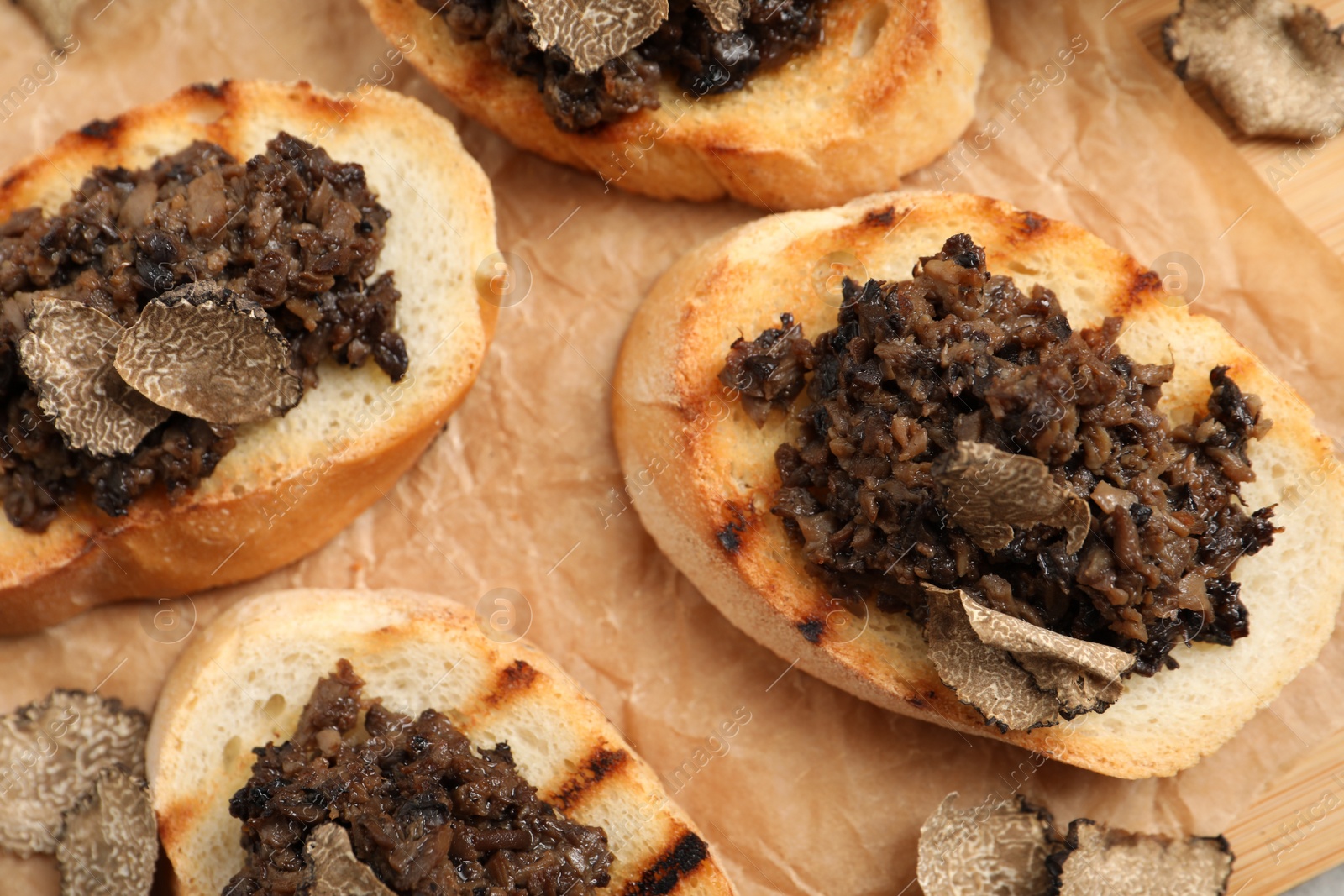 Photo of Delicious bruschettas with truffle sauce on parchment paper, closeup