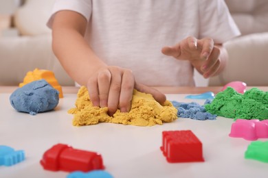 Little boy playing with bright kinetic sand at table indoors, closeup