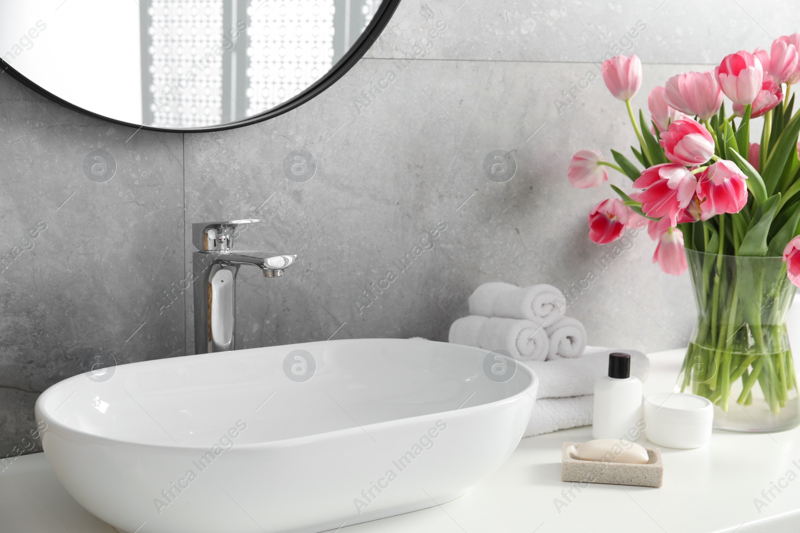 Photo of Vase with beautiful pink tulips and toiletries near sink in bathroom