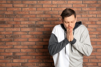 Photo of Man suffering from cold near brick wall. Space for text