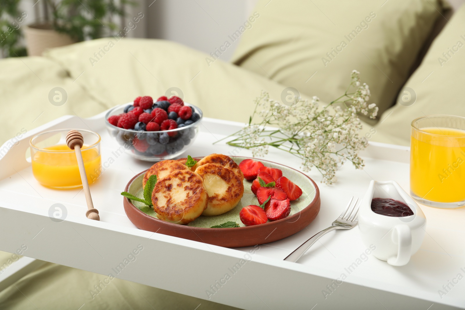 Photo of Tasty breakfast served in bedroom. Cottage cheese pancakes with fresh berries and mint on white tray