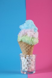 Sweet cotton candy in waffle cone on color background