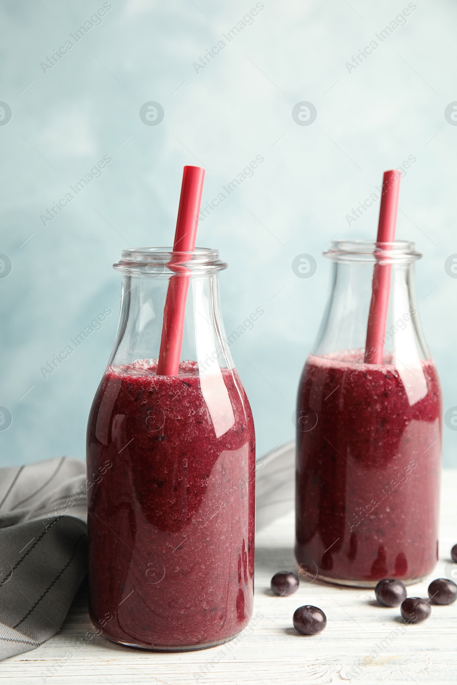 Photo of Bottles with delicious acai smoothie on table against color background