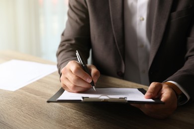 Photo of Businessman signing document at table indoors, closeup