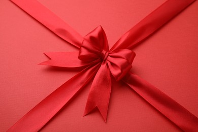 Photo of Bright satin ribbon with bow on red background