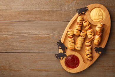 Photo of Cute sausage mummies served with sauce on wooden table, top view with space for text. Halloween party food