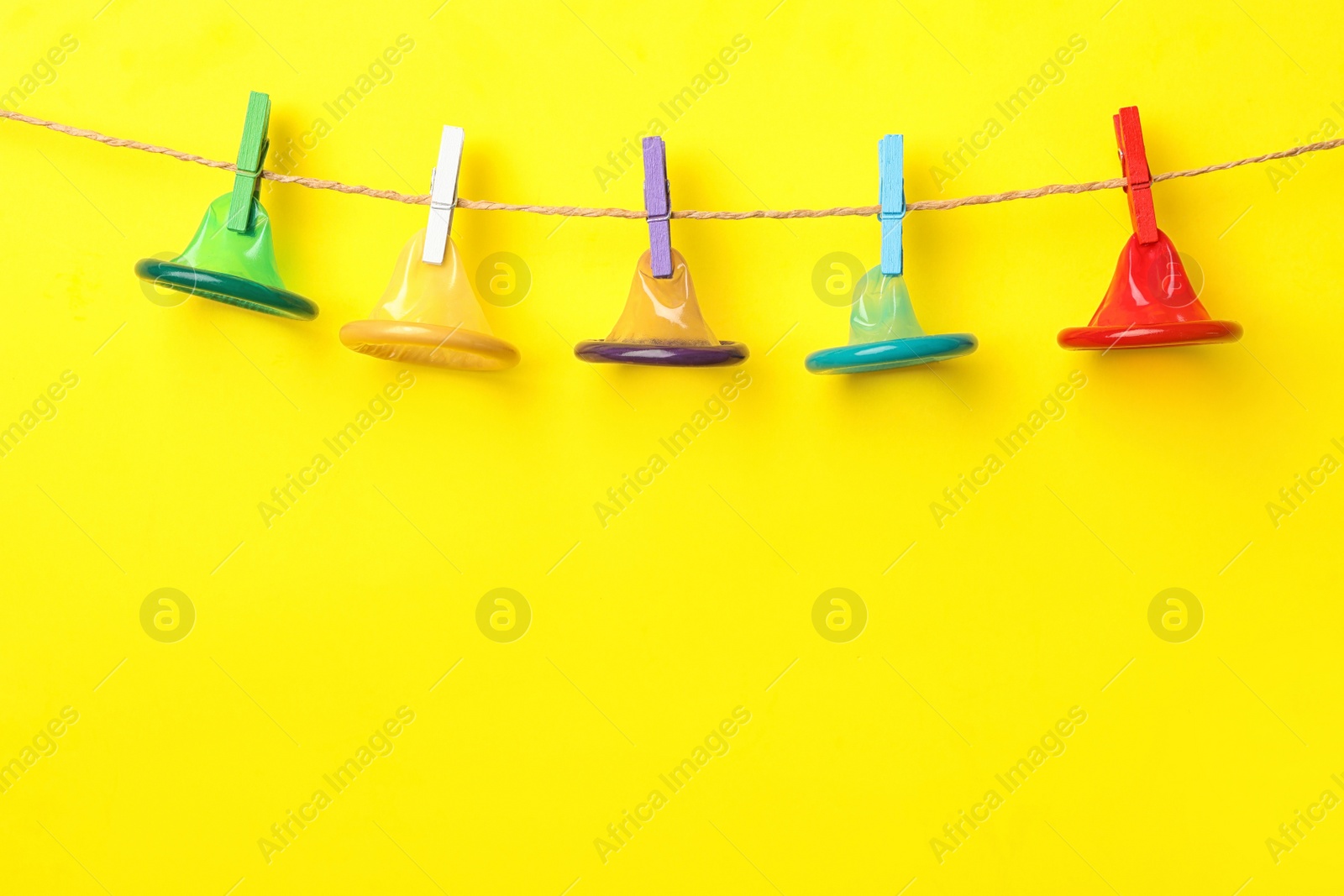 Photo of Colorful condoms hanging on clothesline against yellow background, space for text. Safe sex concept