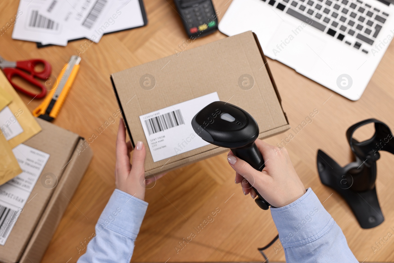 Photo of Parcel packing. Post office worker with scanner reading barcode at wooden table, top view