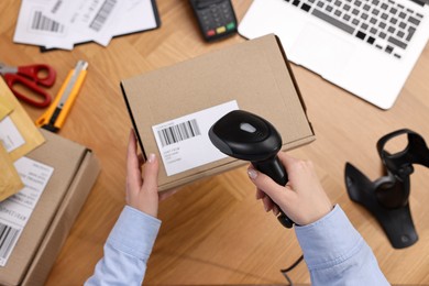 Parcel packing. Post office worker with scanner reading barcode at wooden table, top view