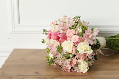 Beautiful bouquet of fresh flowers on wooden table near white wall