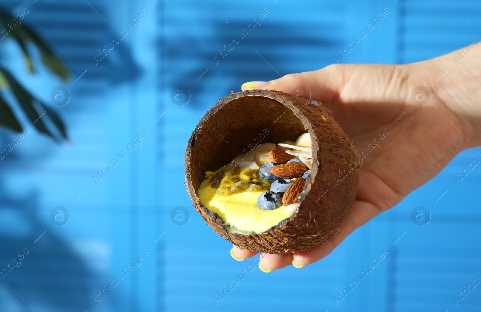 Photo of Woman holding coconut shell with tasty smoothie bowl on blurred background, closeup