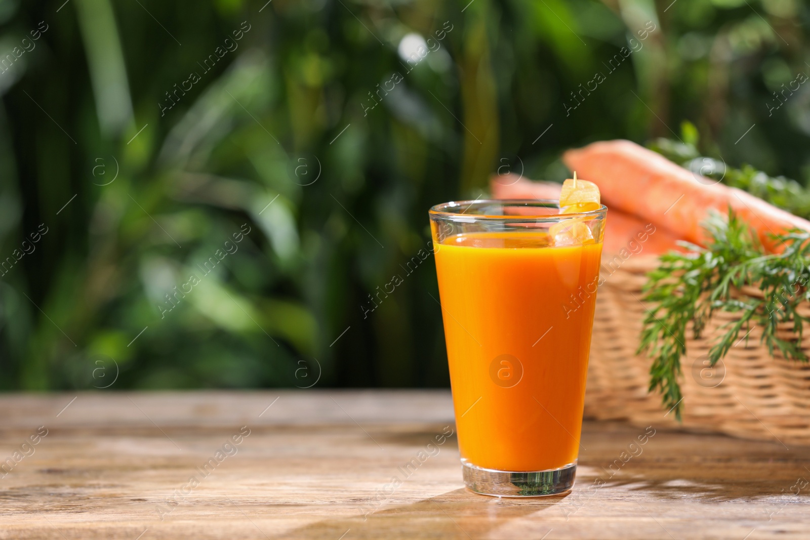 Photo of Tasty juice and carrot on wooden table outdoors. Space for text