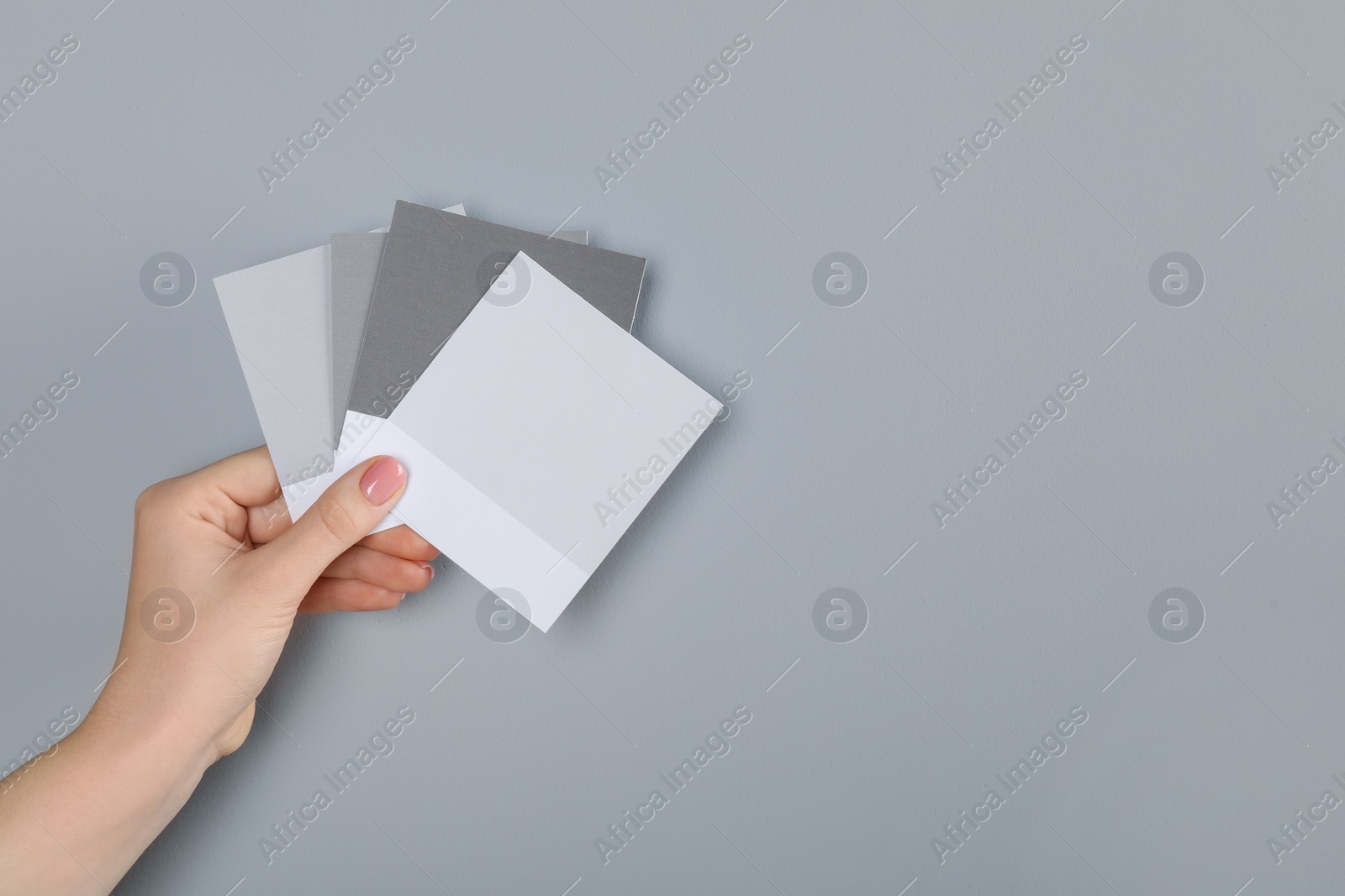 Photo of Woman with color sample cards choosing paint shade near grey wall, closeup. Interior design